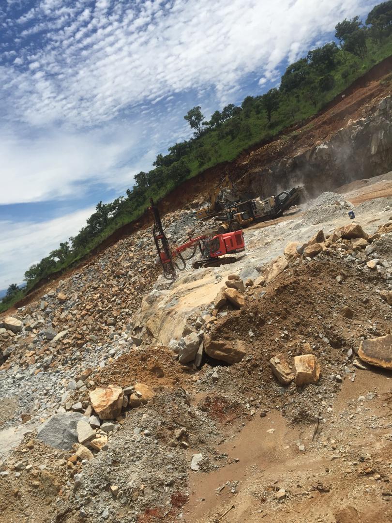 Foreuse et concasseur en activité sur un front de carrière à flanc de colline